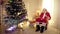 Wide shot joyful bearded old Father Christmas in headphones smiling listening to music sitting on rocking chair indoors