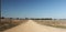 wide shot of long dirt dusty country road leading off into the distance on dry arid drought stricken agricultural farm land, rural