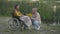 Wide shot of loving Caucasian man reading for paralyzed woman at sunset on river bank. Portrait of young romantic