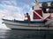 Wide shot of a male sitting at the edge of a boat on the body of water