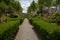 Wide shot of the pathway of a park with hedges flowers and trees on a cloudy day