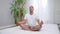 Wide shot portrait of confident young African American man sitting in lotus position on bed in the morning. Handsome