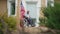 Wide shot portrait of depressed disabled man in wheelchair on porch with USA flag fluttering on house. Sad frustrated