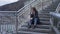 Wide shot portrait of hopeless depressed young woman sitting on city stairs sighing thinking. Beautiful Caucasian