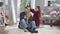 Wide shot portrait of patient young man sitting on soft carpet in living room as playful cute girl making ponytails for