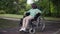 Wide shot portrait thoughtful sad disabled boy in wheelchair in summer park outdoors. Upset lonely Caucasian child alone