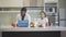 Wide shot of positive African American man working online as daughter having breakfast in kitchen. Portrait of father