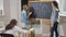 Wide shot of professional teacher and smart schoolgirl standing at chalkboard talking and writing. Intelligent Caucasian