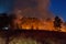 Wide shot of raging wildfire grassfire with emergency vehicle lights in background. Inspiration image for bushfire warning, summer