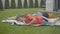 Wide shot of relaxed brunette boy lying on blanket outdoors as cheerful friend or brother rolling to him along green