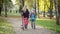 Wide shot of relaxed Caucasian mother and son in coronavirus face masks walking in autumn park with electric scooter and