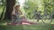 Wide shot side view of relaxed smiling middle aged Caucasian blond woman sitting on blanket in summer park with bicycle