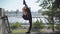 Wide shot side view of young slim flexible woman raising one leg up outdoors. Female Caucasian gymnast warming up in