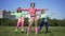 Wide shot slim fit retro woman with hair buns exercising with friends outdoors on sunny meadow. Happy Caucasian fitness