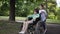 Wide shot smiling disabled boy with girl pushing wheelchair in slow motion outdoors. Happy Caucasian brother and sister