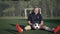 Wide shot smiling motivated sportsman amputee sitting on green grass on sports field with soccer ball. Portrait of