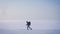 Wide shot of tired backpacker silhouette in profile walking with mountain sticks leftwards on snow.