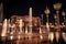 Wide shot of tropical trees and ground water fountains near Emirates Palace at night in Abu Dhabi