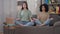 Wide shot of two calm confident slim young women sitting on couch in lotus position with eyes closed. Beautiful Asian