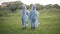 Wide shot of two children in raincoats walking along green summer meadow. Back view of joyful friendly Caucasian friends