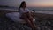 Wide shot of upset beautiful frustrated Caucasian young woman thinking sitting on bed at dusk on sea beach. Portrait of