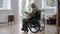 Wide shot of upset frustrated disabled man in wheelchair looking at picture sitting at home indoors. Depressed Caucasian