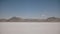 Wide shot of woman walking far away from camera alone in boiling heat at flat salt desert lake in Bonneville Utah.