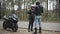 Wide shot of young couple of motorcyclists arguing outdoors on cloudy day. Angry nervous Caucasian woman giving pink