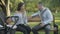 Wide shot of young couple sitting in park with baby stroller and arguing. Conflict of beautiful woman and handsome man