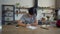 Wide shot of young man writing in slow motion and looking at camera sitting at kitchen table. Web camera POV of