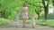 Wide shot of young positive mother strolling outdoors with children. Cute little girl and boy holding hands of parent