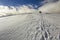 Wide view on the snowy hill with footprints and far away hiker walking up with backpack in the mountains