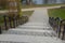 A wide walkway in the park leads directly from the slope down to the pond. has a black metal railing on the handrails. stone and c