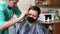 The wife cuts her husband in the kitchen. Husband in a medical mask brushing his hair with a brush. Haircut at home in self-