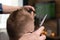 Wife cutting husbands hair at home in front of TV . Scissors in focus