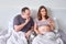 Wife looks at the phone on the bed next to her husband, relationship problems during pregnancy