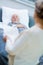 Wife stands in front of the bed of her sick husband and holds an adult diaper