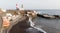 Wild black sand beach with cave and small boats and a port with lighthouse in volcano coastline. Volcanic soil in rural village in