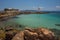 The wild coast of Aegina island with clear and blue waters of Mediterranean sea and the old small lighthouse in the background, in