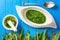 Wild garlic leaves with mortar, spoon and garlic soup in white plate on blue wooden background, healthy lifestyle, seasonal spring