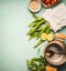 Wild garlic in paper with cooking pot and spoon, and ingredients on kitchen table background, top view