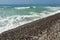 Wild natural beach with mostly dark pebble stones wet from sea, sky in background