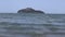 Wind blowing over sea waves on the beach in daytime. The waves hitting the empty sandy beach. Beach with a mountain background.