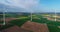 Wind farm stands in the green field, wind power generator on the background of the blue sky and floating clouds, Europe