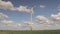 Wind farm stands in the green field, wind power generator on the background of the blue sky and floating clouds, sunny