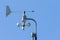 A wind gauge for wind strength and direction on a pipe against a blue sky.