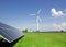 Wind generator of electricity from three blades and solar panels of a battery of photocells clouds and a blue sky green grass