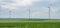 Wind park with several modern renewable energy wind turbines, agricultural field in the front, cloudy day, landscape, panorama