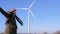 Wind power turbines, young woman in sunglasses shows finger on windmill on sky background