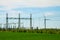 Wind turbine farm and substation electricity power line in landscape with green grass and blue sky.